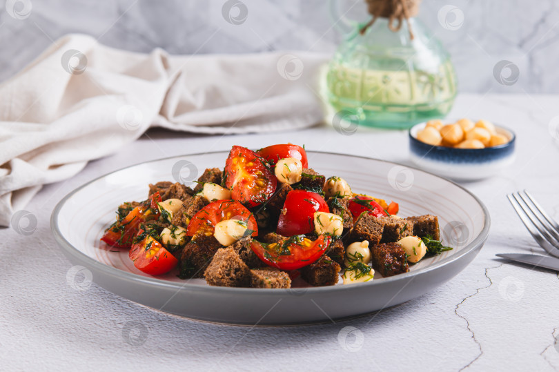 Скачать Салат из ржаного хлеба, помидоров черри и копченого сыра на тарелке на столе фотосток Ozero
