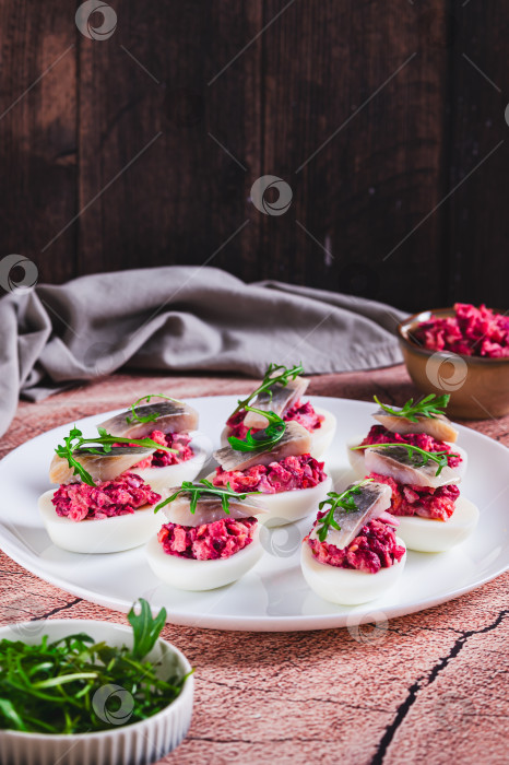 Скачать Половинки яиц, фаршированные сельдью под шубой, на тарелке на столе, вид сверху фотосток Ozero