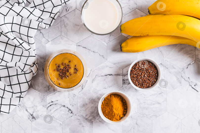 Скачать Смузи из кокосового молока, банана, куркумы и семян льна в стеклянном бокале, вид сверху фотосток Ozero
