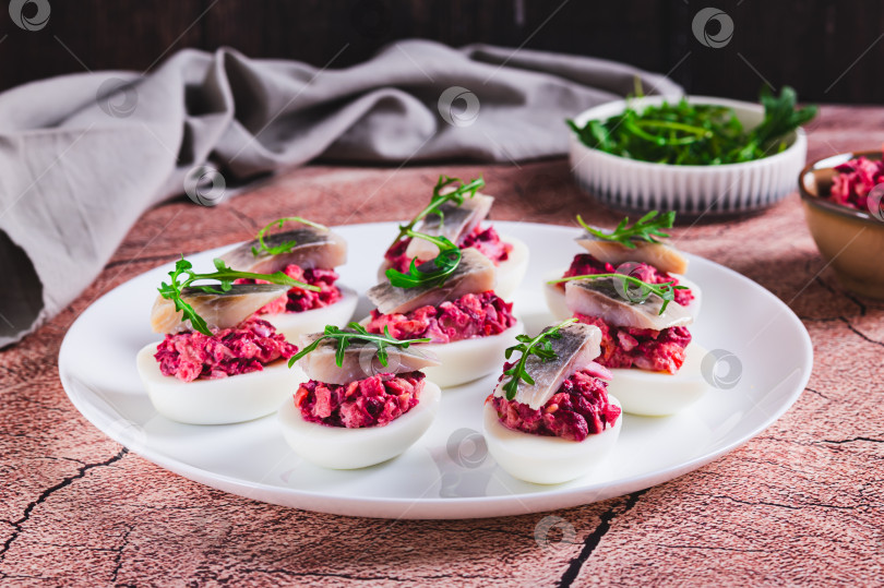 Скачать Половинки яиц, фаршированные сельдью под шубой, на тарелке на столе фотосток Ozero