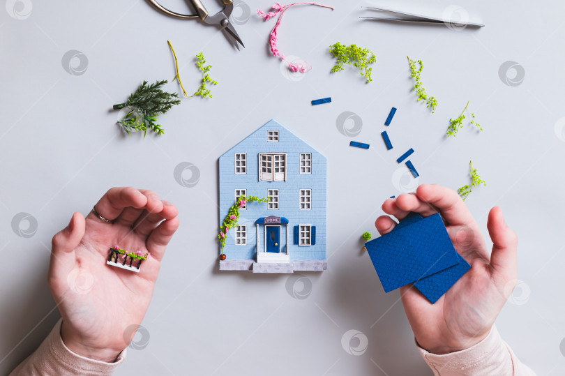 Скачать Детали для сборки модели домика в детских ладошках на синем фоне, вид сверху фотосток Ozero