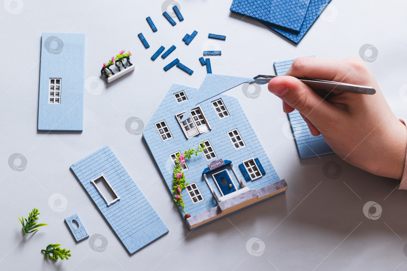 Скачать Детская рука держит пинцетом часть крыши игрушечного домика. фотосток Ozero