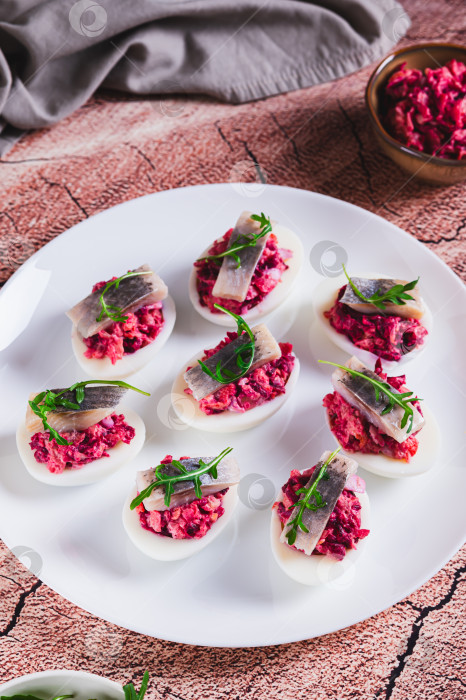 Скачать Яйца, запеченные с овощным салатом, кусочком сельди и рукколой на тарелке, подаются на стол в вертикальном положении фотосток Ozero