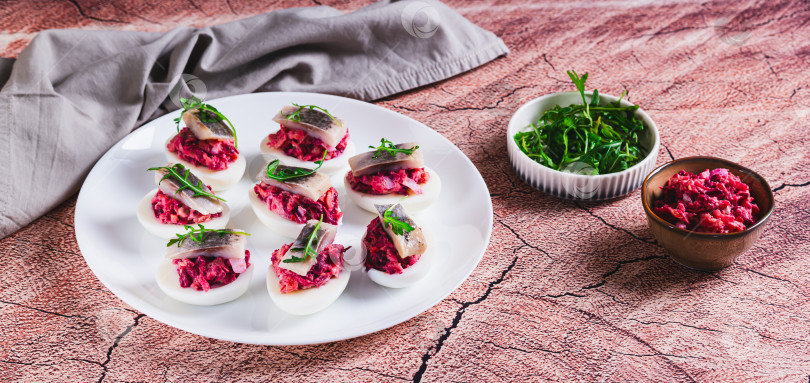 Скачать Половинки яиц, фаршированные сельдью под шубой, на тарелке на столе веб-баннер фотосток Ozero
