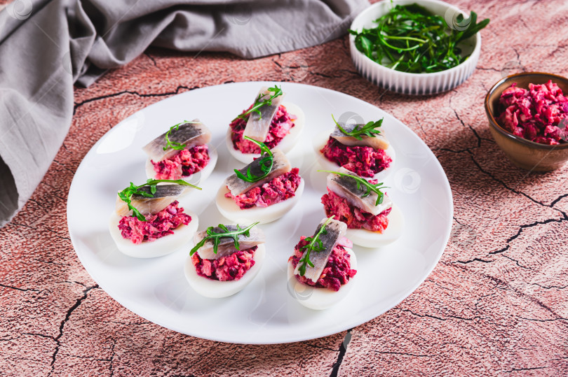 Скачать Подаем на стол на тарелке яйца, запеченные с овощным салатом, кусочком сельди и рукколой фотосток Ozero