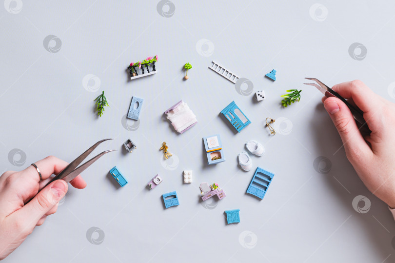 Скачать Миниатюрные детали игрушечного домика и детские ручки с пинцетом на синем фоне фотосток Ozero