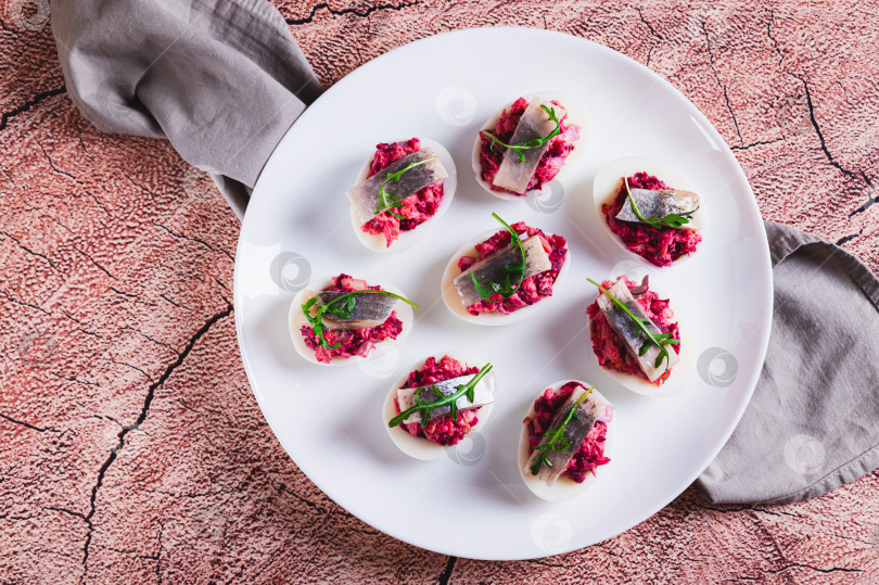 Скачать Крупный план половинок яиц, фаршированных сельдью под шубой, на тарелке на столе, вид сверху фотосток Ozero