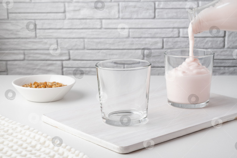 Скачать Заливка из домашнего кефира, пахты или йогурта с пробиотиками. Клубничный йогурт вытекает из стеклянной бутылки на светлом фоне. Холодный кисломолочный напиток с пробиотиками. Модные блюда и напитки фотосток Ozero