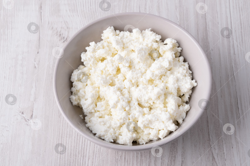 Скачать Свежий творог лежит в миске на светлом деревянном столе фотосток Ozero