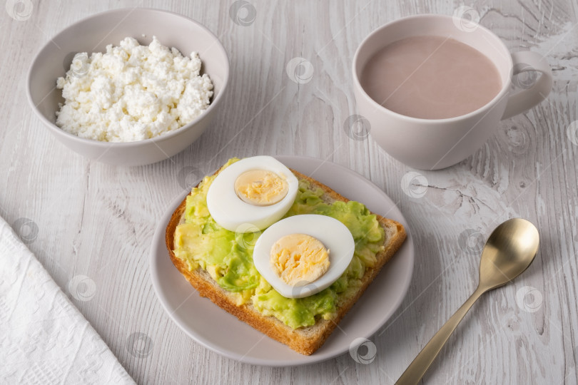 Скачать Полезный завтрак с тостами, вареными яйцами, творогом, хлебом и горячими напитками подается на деревянном столе в утреннем свете фотосток Ozero