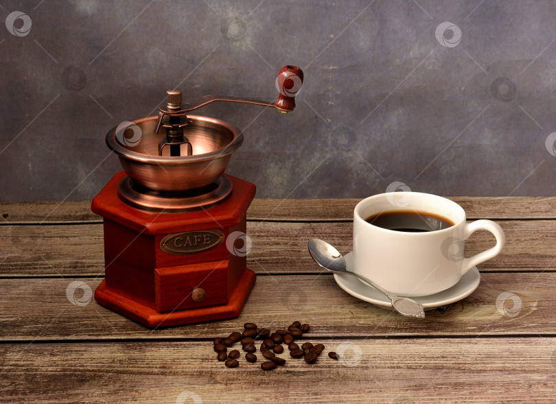 Скачать Чашка горячего черного кофе на блюдце с ложечкой, обжаренные зерна и ручная кофемолка на деревянном столе. фотосток Ozero