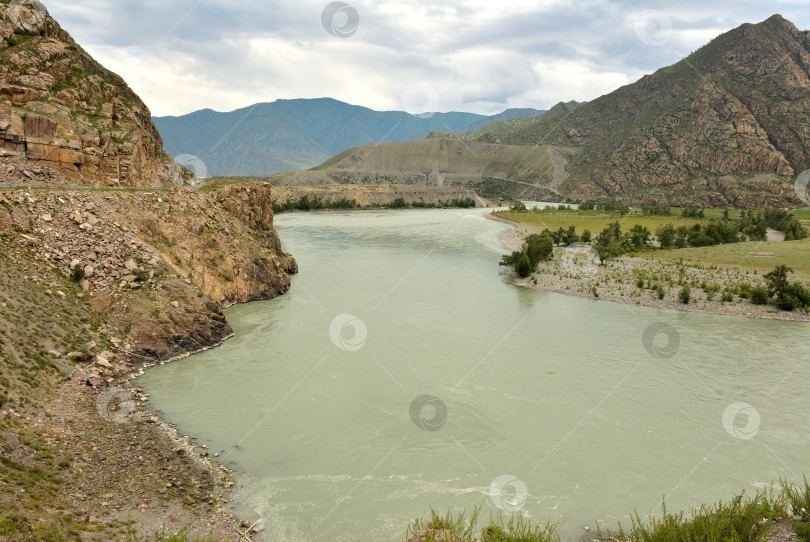 Скачать Изгибы русла красивой широкой реки, текущей у подножия высокого утеса по горной долине в пасмурный летний день. фотосток Ozero