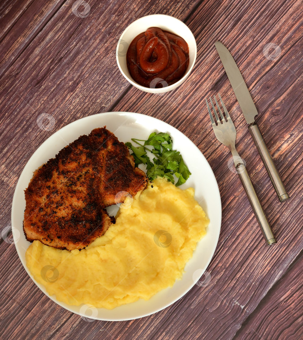 Скачать Свиная отбивная в панировке с картофельным пюре и томатным соусом на деревянном столе. фотосток Ozero
