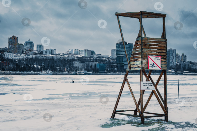 Скачать Спасательная вышка с предупреждающими знаками у реки Дон на фоне зимнего города фотосток Ozero