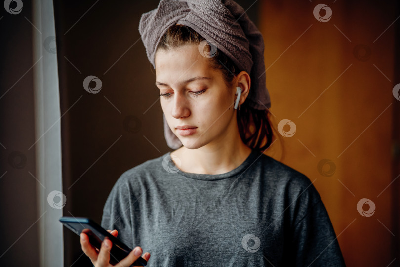 Скачать Девочка-подросток смотрит в свой телефон у окна после душа фотосток Ozero