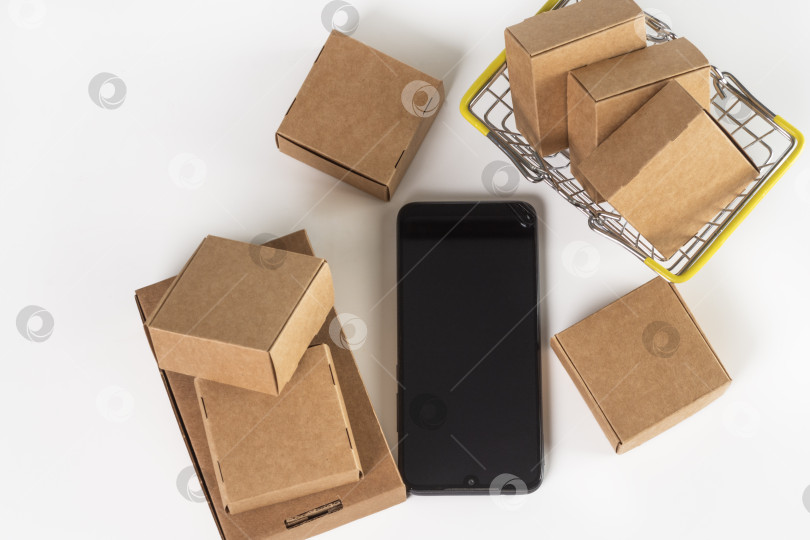 Скачать Картонные коробки разных размеров, корзина для покупок и смартфон на белом фоне. Доставка с торговых площадок и интернет-магазинов. Плоская выкладка. Вид сверху фотосток Ozero