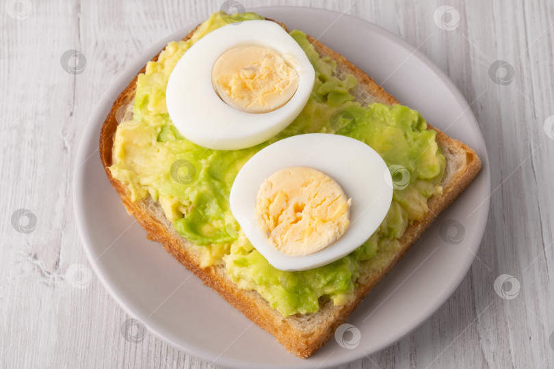 Скачать Вкусные тосты с пюре из авокадо и нарезанными ломтиками вареными яйцами подаются на тарелке фотосток Ozero