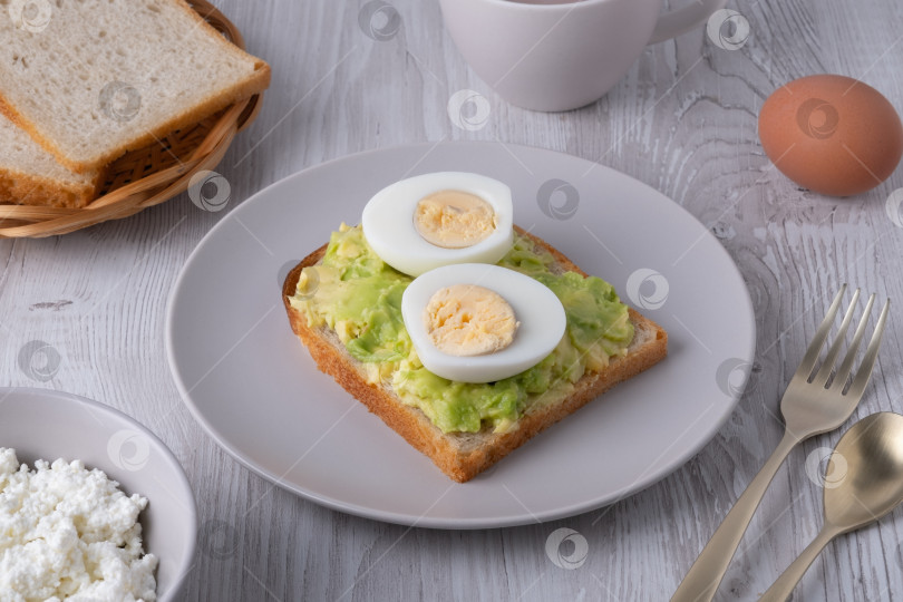 Скачать Полезный завтрак с тостами, вареными яйцами, творогом, хлебом и горячими напитками подается на деревянном столе в утреннем свете фотосток Ozero