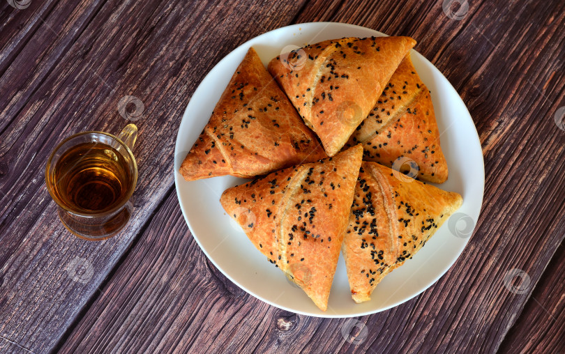Скачать Тарелка с несколькими традиционными мясными пирогами, самсой и чашкой горячего чая на деревянном столе. Вид сверху, плоская тарелка. фотосток Ozero