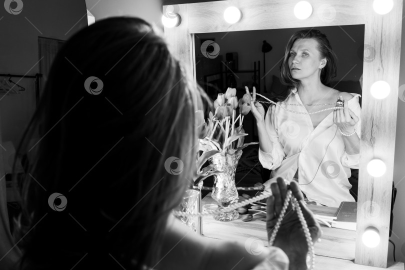 Скачать Женщина, Надевающая Жемчужное Ожерелье, Смотрит На Отражение В Голливудском Зеркале фотосток Ozero