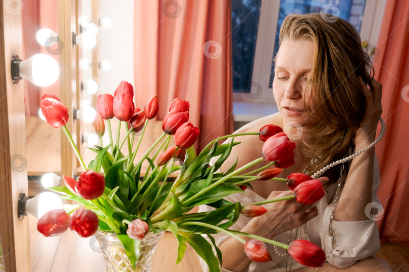 Скачать Женщина трогает волосы у голливудского зеркала с красными тюльпанами фотосток Ozero