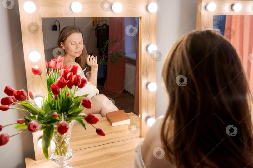 Скачать Задумчивая женщина у зеркала для макияжа с красными тюльпанами фотосток Ozero