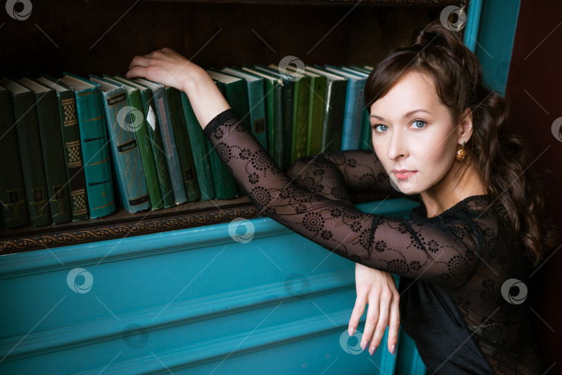 Скачать Стильная женщина, опирающаяся руками на книжную полку в Классической библиотеке фотосток Ozero