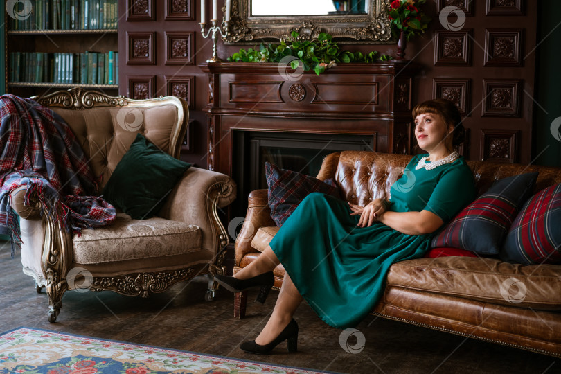 Скачать Утонченная женщина в зеленом платье мечтает у камина в роскошном доме фотосток Ozero