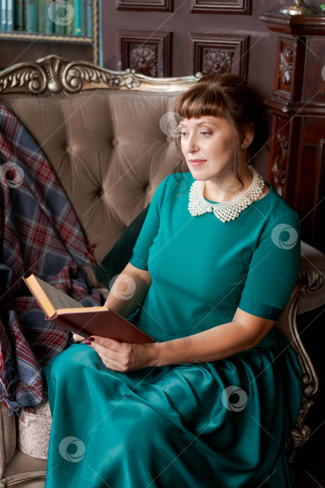 Скачать Элегантная женщина в зеленом платье читает книгу в классическом библиотечном интерьере фотосток Ozero