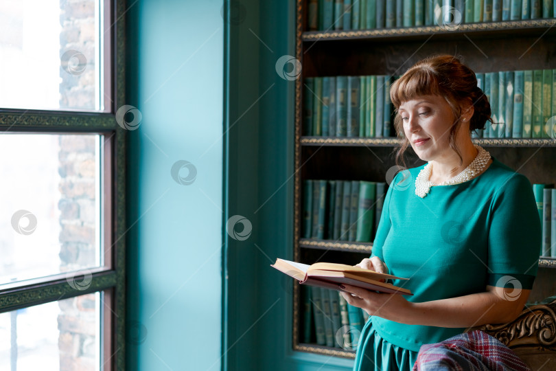 Скачать Элегантная женщина читает книгу в библиотеке при свете окна фотосток Ozero