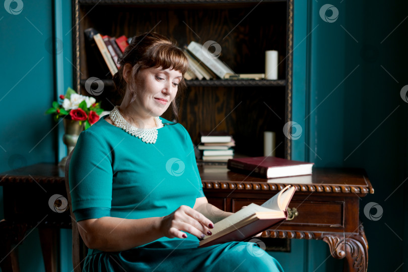 Скачать Элегантная женщина читает книгу за старинным деревянным столом в библиотеке фотосток Ozero