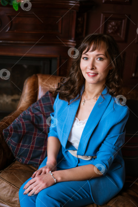 Скачать Сияющая деловая женщина в синем костюме улыбается на кожаном диване в классическом офисе фотосток Ozero