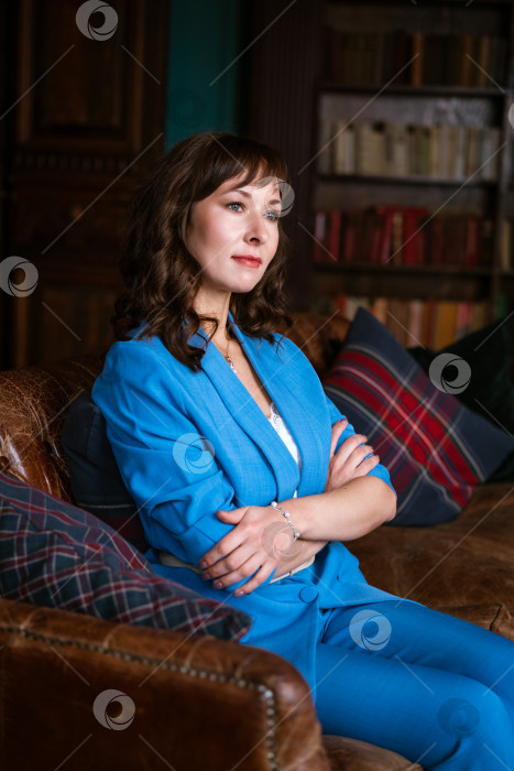 Скачать Задумчивая деловая женщина в синем костюме сидит на диване в классическом офисе фотосток Ozero