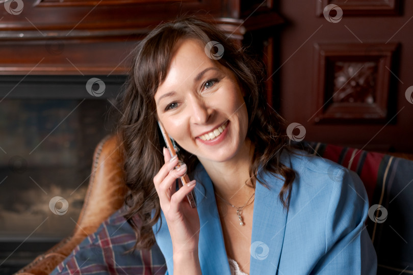 Скачать Жизнерадостная деловая женщина разговаривает по смартфону в классическом офисном интерьере фотосток Ozero