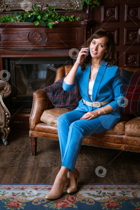 Скачать Деловая женщина в синем костюме разговаривает по смартфону, сидя на кожаном диване фотосток Ozero