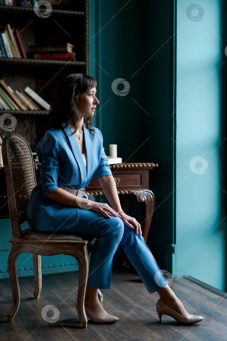 Скачать Элегантная деловая женщина в синем костюме сидит у окна в классическом офисе фотосток Ozero