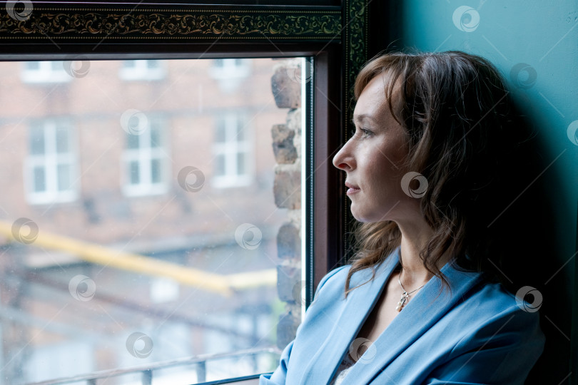 Скачать Задумчивая женщина, выглядывающая из окна в современном городском интерьере фотосток Ozero