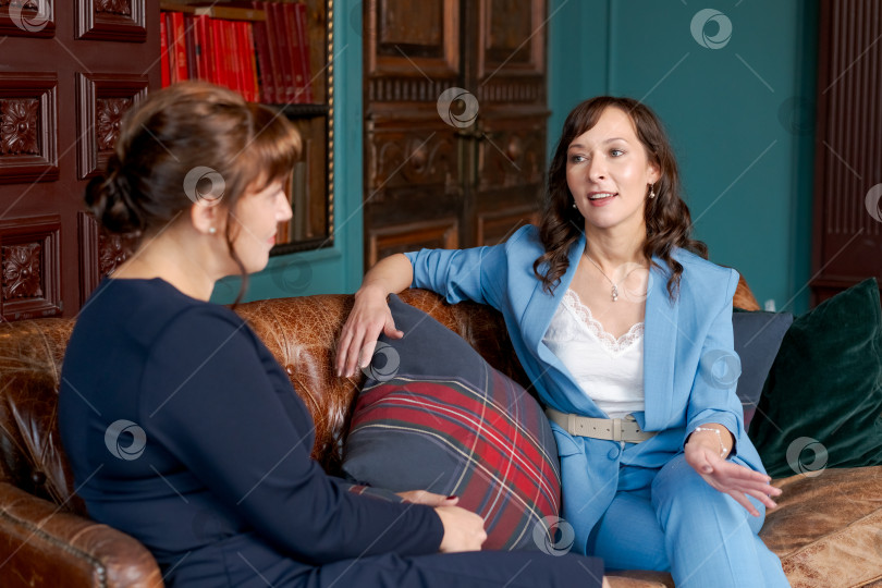 Скачать Две профессиональные женщины увлеченно беседуют на диване в классическом офисе фотосток Ozero