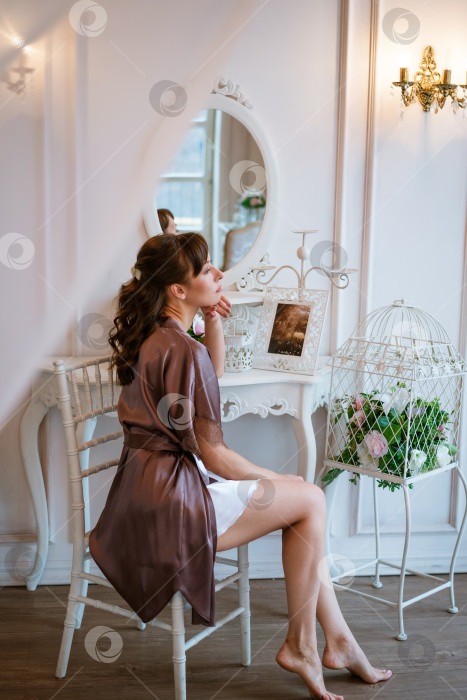 Скачать Элегантная молодая женщина в шелковом халате сидит за винтажным туалетным столиком фотосток Ozero