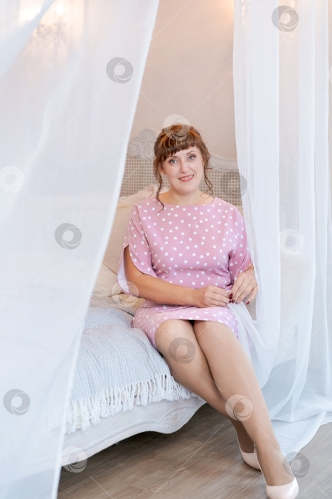 Скачать Сияющая женщина в розовом платье в горошек сидит на кровати с балдахином фотосток Ozero