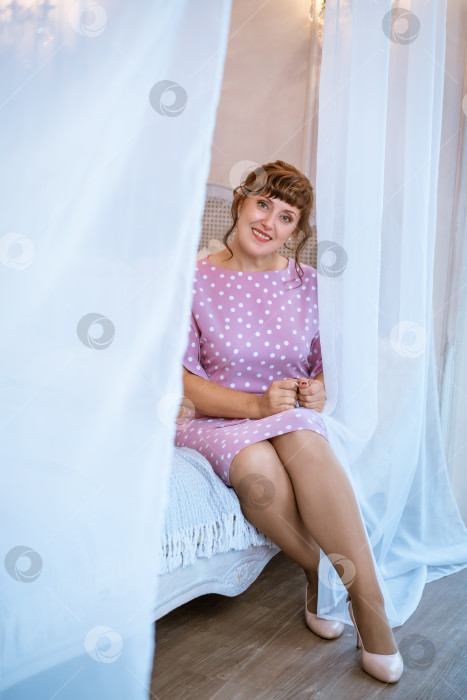 Скачать Счастливая женщина в розовом платье в горошек сидит на кровати с белым балдахином фотосток Ozero