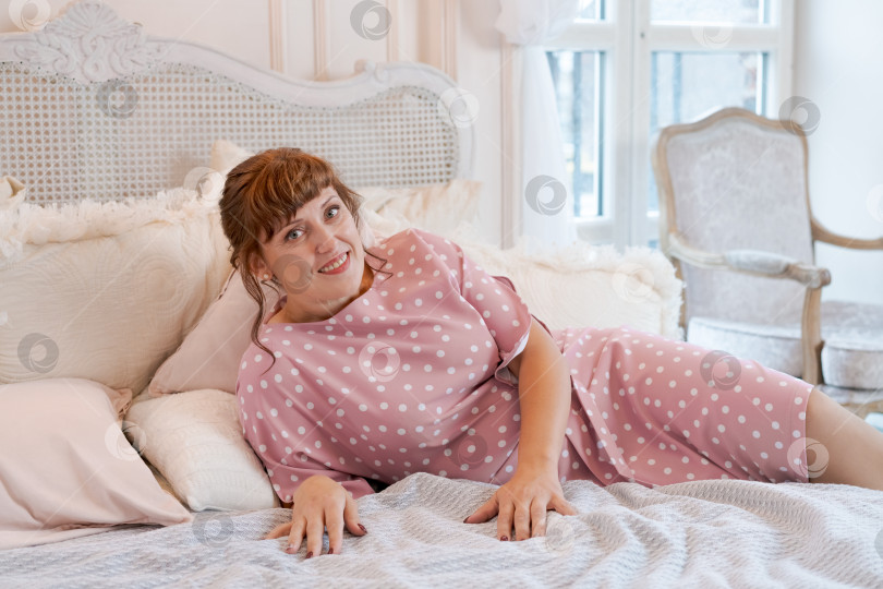 Скачать Счастливая женщина в розовом платье в горошек лежит на кровати в ярком интерьере фотосток Ozero