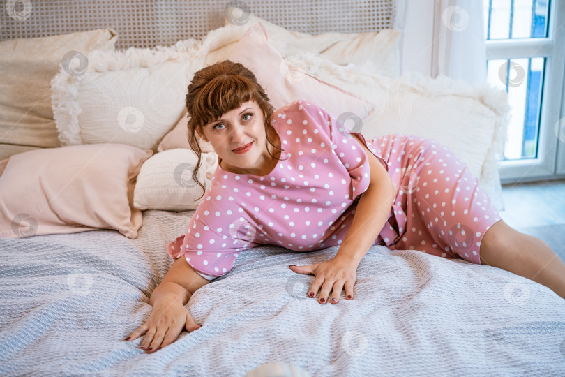 Скачать Очаровательная женщина в розовом платье в горошек расслабляется на кровати фотосток Ozero