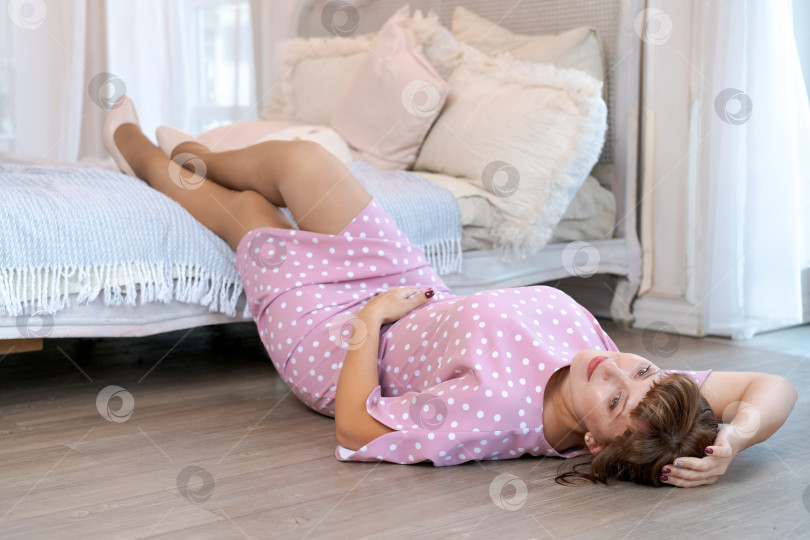 Скачать Радостная женщина в розовом платье в горошек лежит на полу у кровати фотосток Ozero