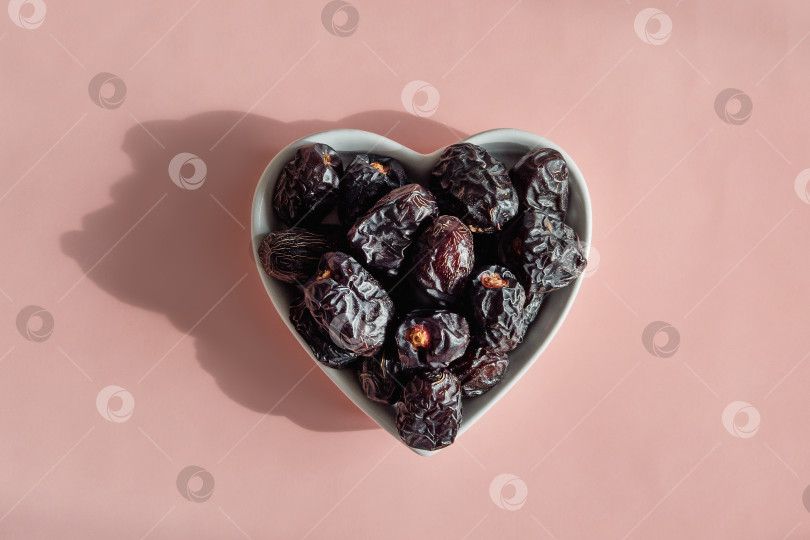 Скачать В миске в форме сердца лежат темные, сморщенные сушеные финики фотосток Ozero