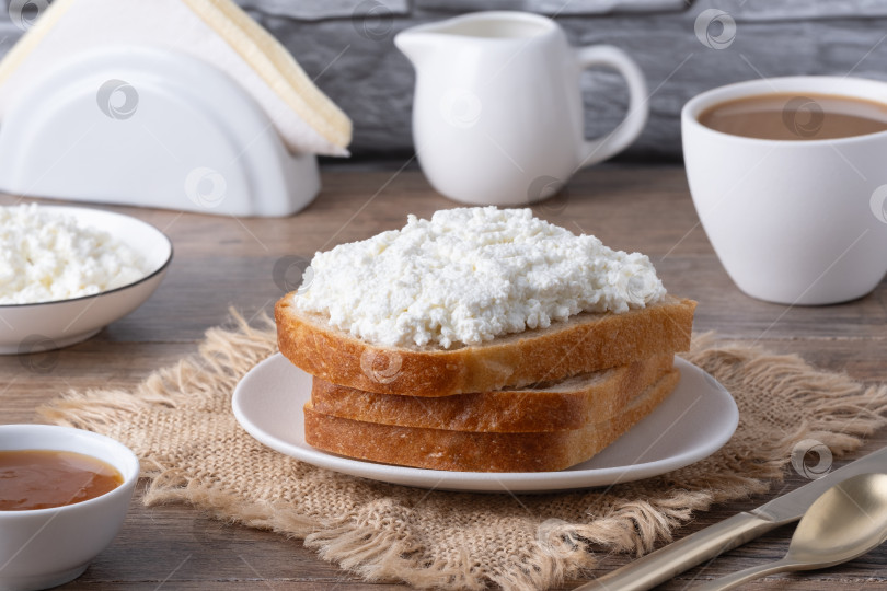 Скачать Сервировка завтрака с хлебом, творогом, кофе и джемом на деревянном столе в уютной кухонной обстановке фотосток Ozero