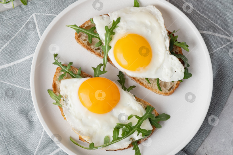 Скачать Завтрак с яйцами на тосте и свежей рукколой подается на белой тарелке фотосток Ozero