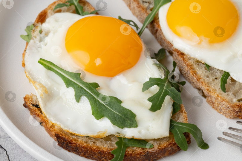 Скачать Завтрак с яйцами на тосте и свежей рукколой подается на белой тарелке фотосток Ozero