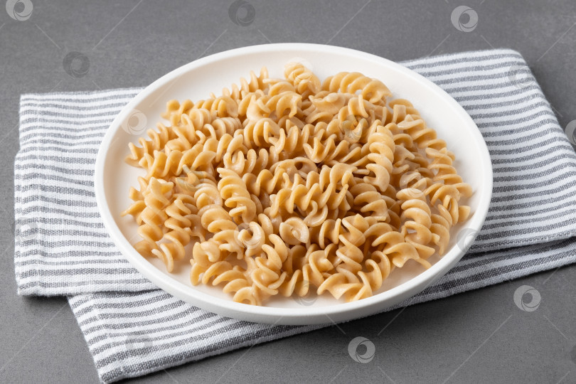 Скачать Паста подается на белой тарелке, накрытой полосатым кухонным полотенцем, к обеденному столу в дневное время фотосток Ozero