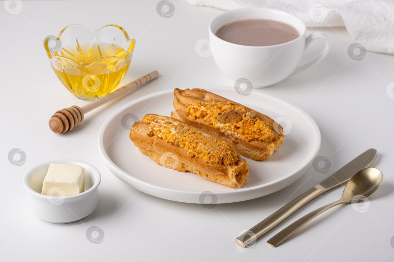 Скачать Две выпечки на тарелке с горячим напитком, медом и сливочным маслом на белом столе фотосток Ozero